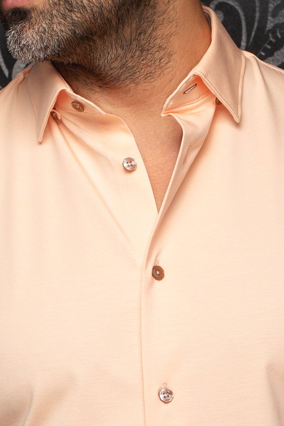 Détail du col d’une chemise pêche avec tissu lisse et boutons bruns lustrés pour homme par Au Noir