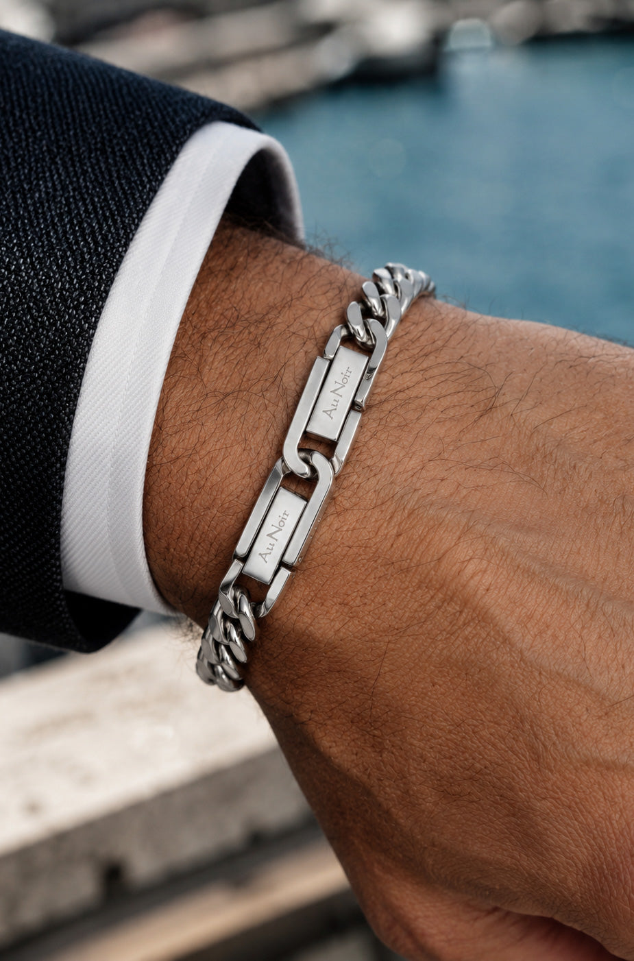 Bracelet gourmette argenté porté au poignet, avec deux plaques rectangulaires gravées Au Noir pour homme, détail
