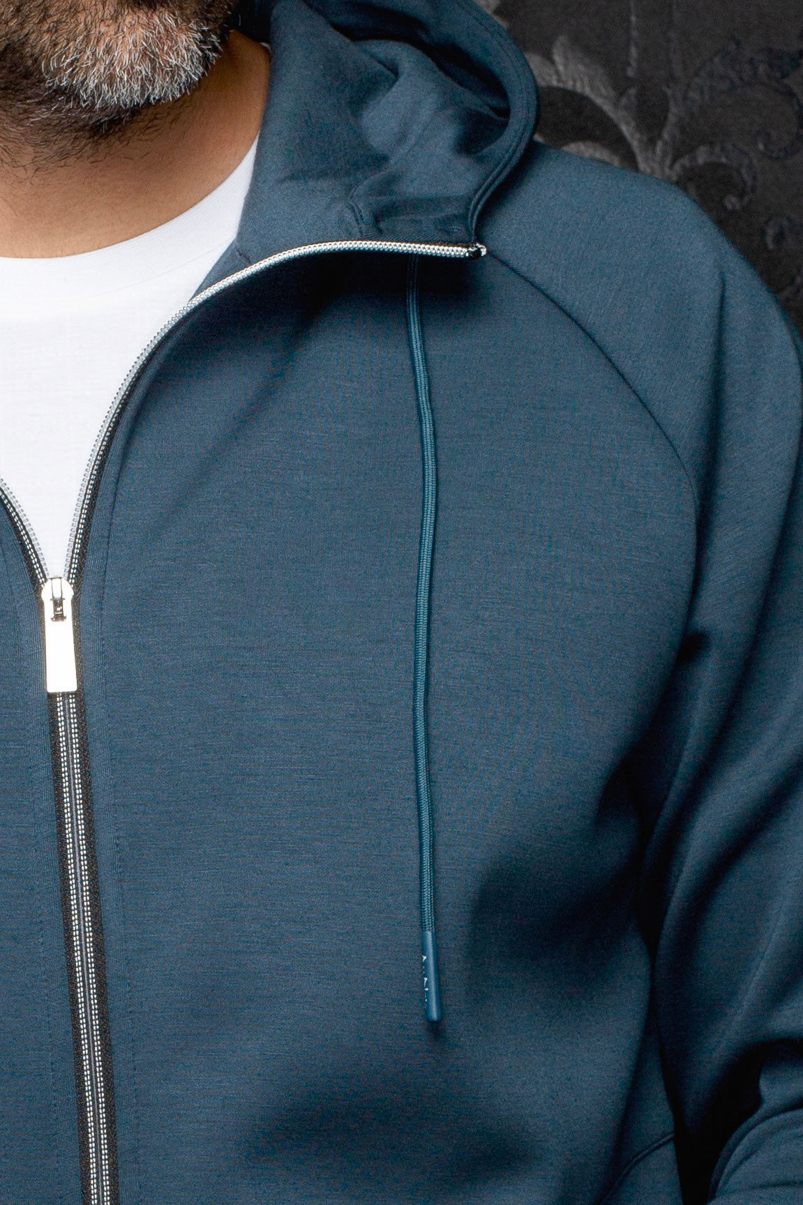 Gros plan d’une veste sport à capuchon sarcelle avec fermeture argentée, cordon et couture raglan pour homme par Au Noir