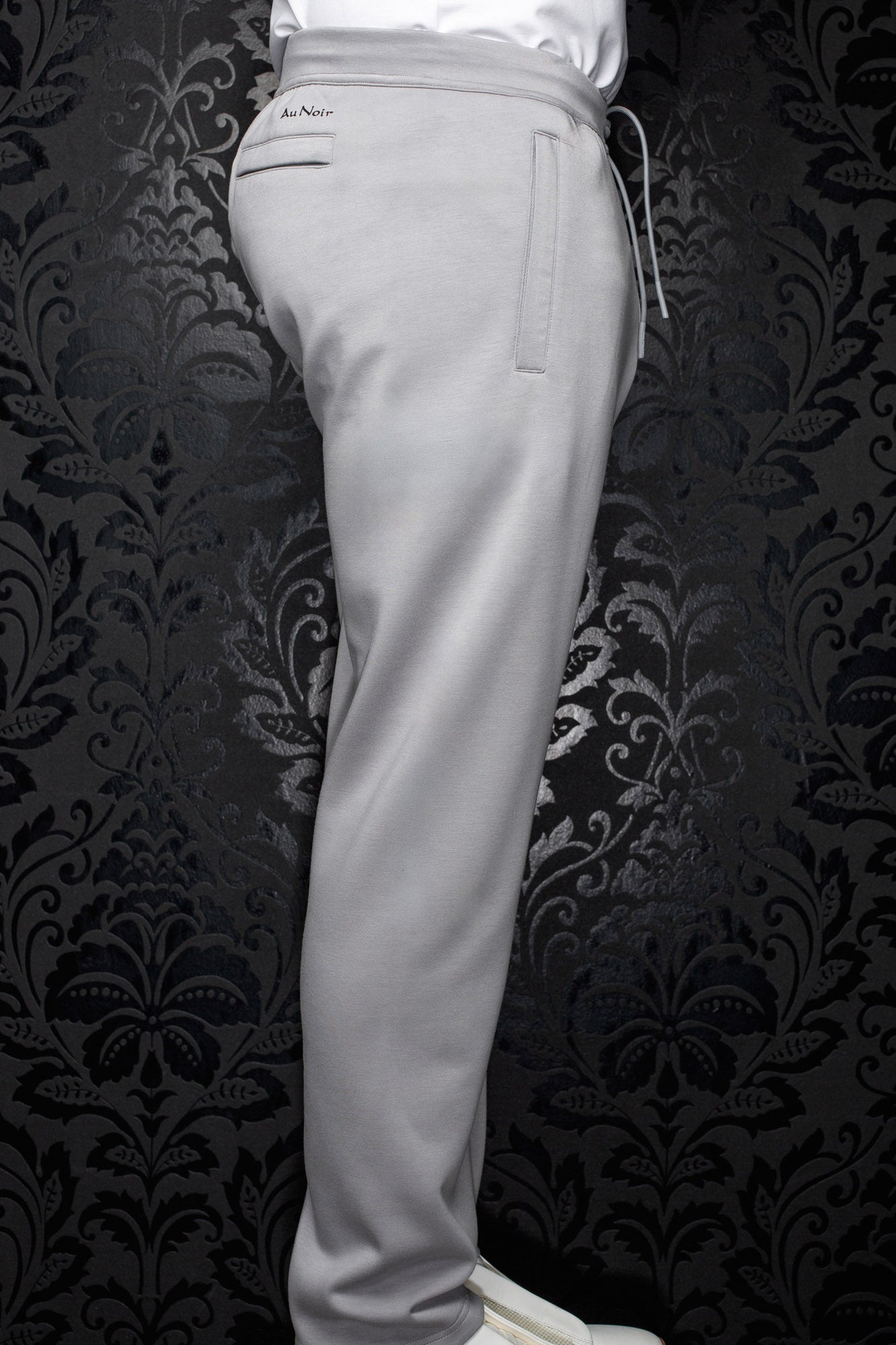 Men's light gray jogging pants side view with elastic waistband, drawcord, welt pockets, and full leg by Au Noir