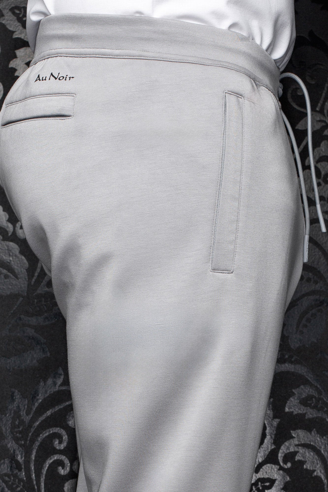 Men's light gray jogging pants waistband, drawcord, welt pockets, and small black Au Noir logo, close-up