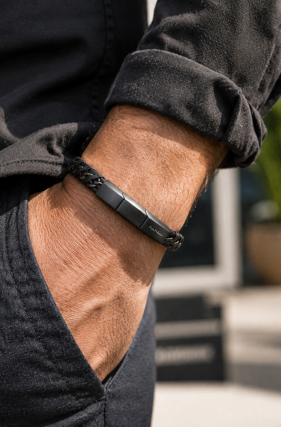 Bracelet noir tressé porté au poignet, avec fermoir rectangulaire à logo et fini foncé pour homme par Au Noir, détail