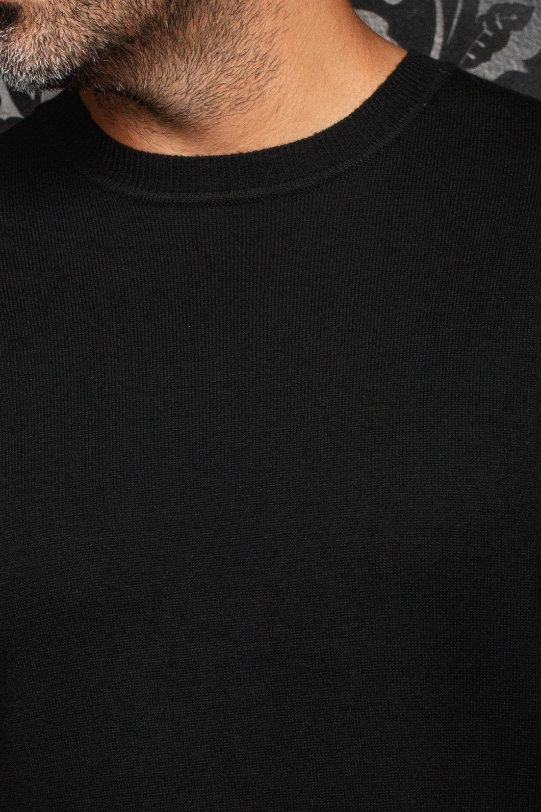 Au Noir men's black fine-knit crewneck cashmere sweater showing the ribbed collar and plain front, close-up