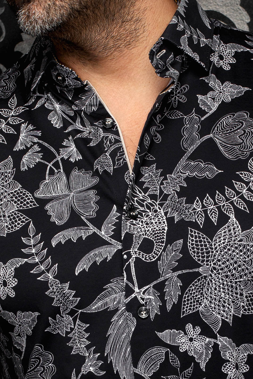 Col et patte d’une chemise noire à motif floral blanc et boutons noirs pour homme par Au Noir, en gros plan