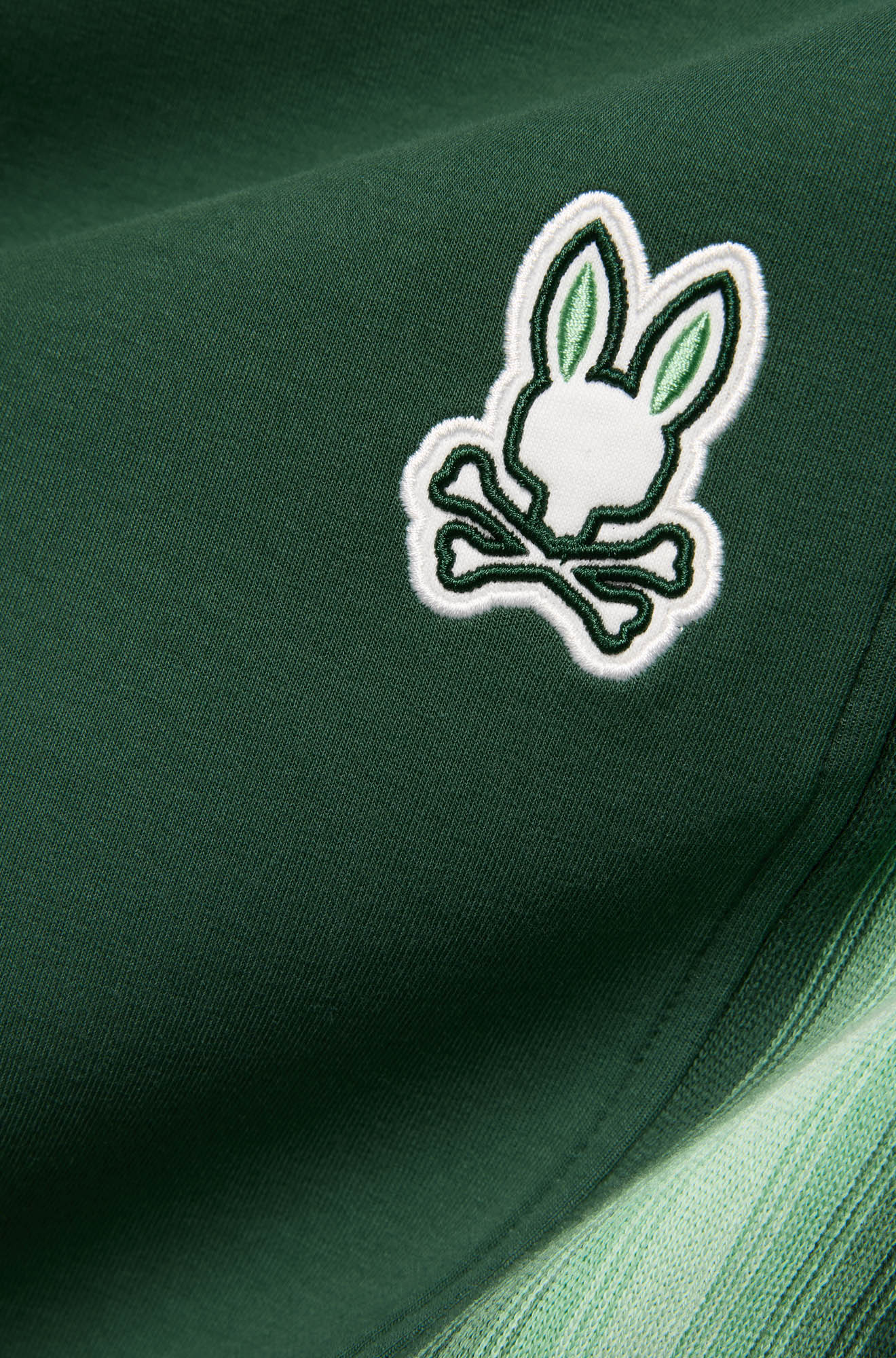 Gros plan du pantalon jogging vert foncé avec bande latérale pâle et écusson lapin brodé pour homme par Psycho Bunny