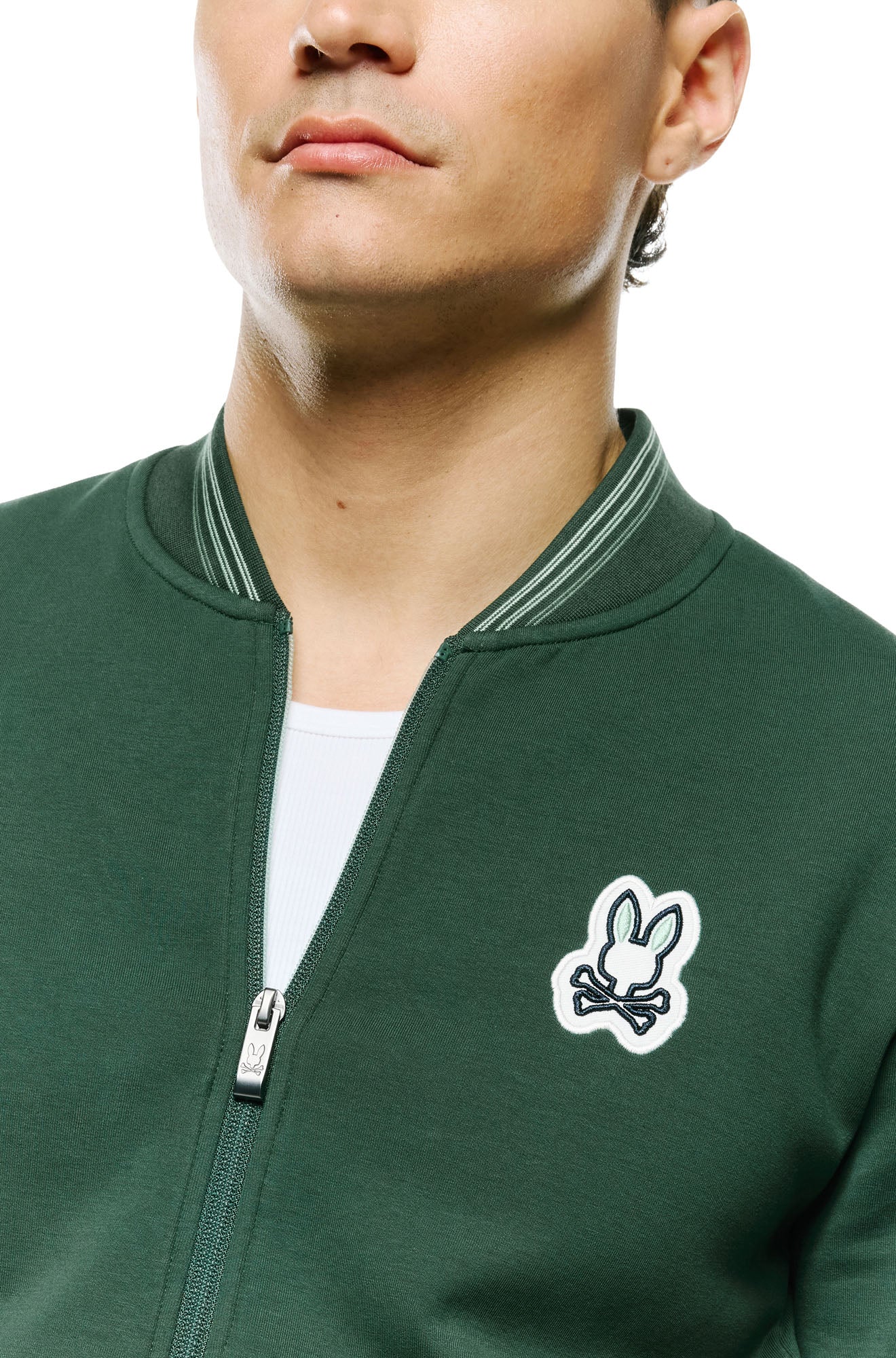 Gros plan du col, de la tirette et de l’écusson lapin sur le jacket bomber verte pour homme par Psycho Bunny
