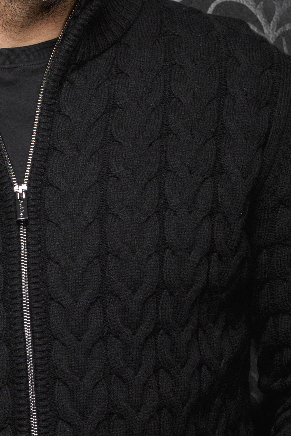 Au Noir men's black cable-knit zip merino jacket showing silver-tone zipper and raised knit pattern, close-up